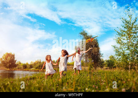 Happy little girls running avec kite en parc d'été tandis que leur mère les aide. Les enfants s'amusant jeux en plein air. Temps de la famille Banque D'Images