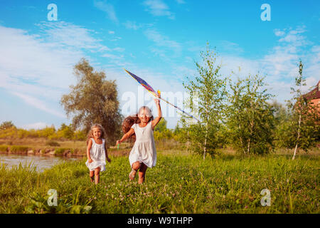 Happy little girls avec kite s'exécutant sur meadow en parc d'été. Les enfants s'amusant jeux en plein air. Soeurs appréciant les jours fériés Banque D'Images