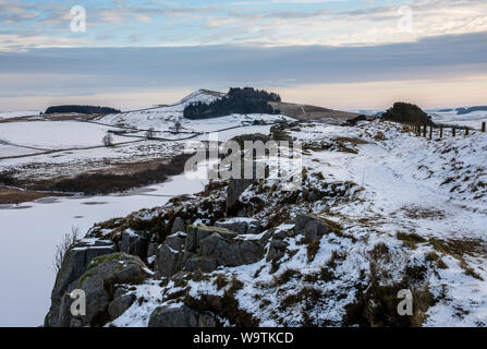 Neige de l'hiver se trouve sur le mur d'Hadrien le chemin tel qu'il traverse au-dessus d'une falaise Highshield Crag Lough gelé lac près de une fois brassé dans le Northumberland. Banque D'Images