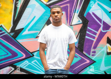 Un jeune homme pose devant un mur d'art graffiti sur une rue de ville de Spitalfields, E1 Banque D'Images