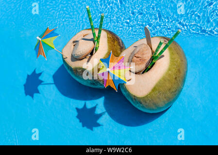 Cocktail de noix de coco fraîche deux cocotiers sur fond bleu avec des parasols. Banque D'Images