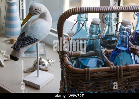 Close up de plusieurs bouteilles d'eau en verre dans un panier en osier et un oiseau en bois décoratif sur le rebord, selective focus Banque D'Images