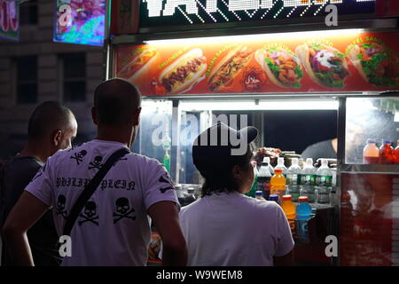 New York City, NY / USA - Le 28 juin 2019 : Plusieurs hommes l'achat d'un vendeur de produits halal dans la nuit Banque D'Images