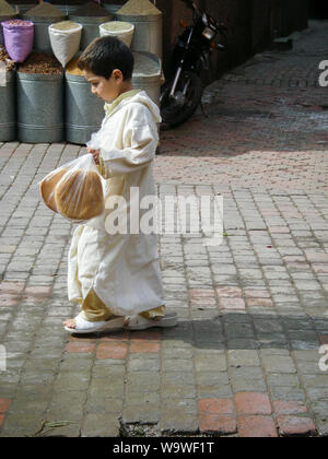 Marrakech, Maroc April 02,2010 : jeune garçon marocain blanc en vêtements traditionnels et de grandes chaussures est la marche dans le souk et porte le pain Arabe Banque D'Images