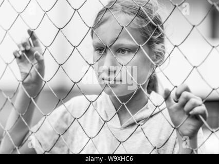 Portrait of young caucasian girl derrière le filet. Les questions sociales, la dépression et l'enfant la tristesse. Tourné en noir et blanc. Banque D'Images