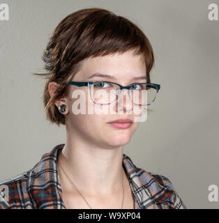 Une jolie jeune femme dans une chemise de flanelle occasionnels la caméra donne une apparence de gravité et d'inquiétude, dans un studio photo avec un fond gris. Banque D'Images