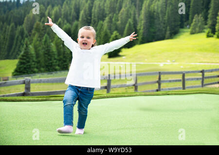 Happy Little Girl s'exécutant sur pré vert dans les montagnes Banque D'Images