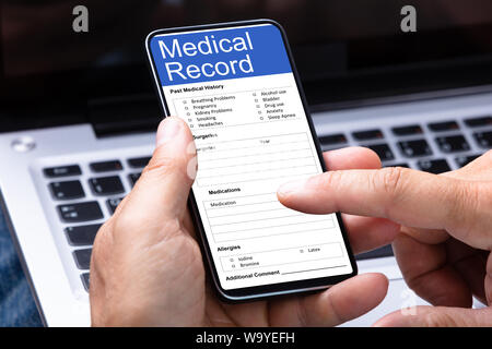 La main de la personne remplissant le formulaire d'information patient sur ordinateur portable sur smartphone Banque D'Images