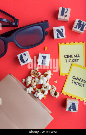 Sac d'artisanat avec popcorn cinéma 3D avec des cubes en bois billets lunettes sur fond rouge Texte flatlay créative Banque D'Images