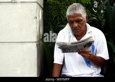 ANTIPOLO CITY, PHILIPPINES - le 12 août 2019 : Adulte ou senior homme de son pays se détendre et de s'asseoir sur un banc de parc et lire un journal. Banque D'Images