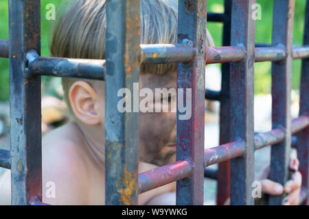 Cette image appelle à la protection des droits de l'homme et la lutte contre la violence. 5 ans garçon est assis derrière les barreaux et regarde. con Banque D'Images