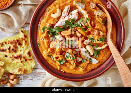 Soupe Mulligatawny épicé chaleureux avec la viande de poulet et le lait de coco saupoudré de cajou frits dans un bol avec chapati sur une table en bois blanc, un Indien Banque D'Images