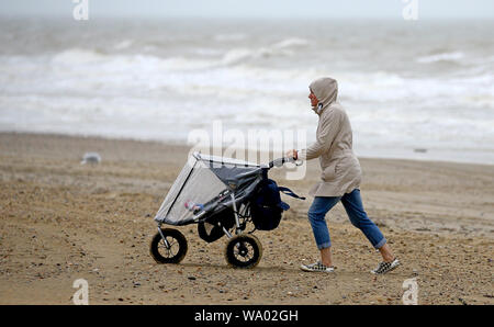 Une dame pousse un buggy le long de Camber Sands dans l'East Sussex en cas de mauvais temps. Banque D'Images