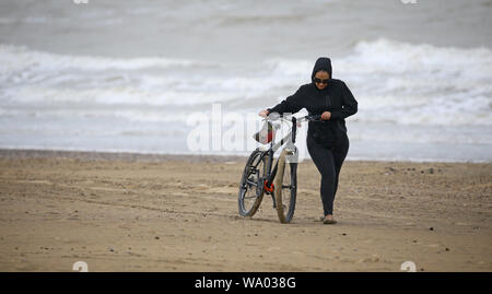 Une dame pousse son vélo le long d'une plage vide dans le carrossage, East Sussex, en cas de mauvais temps. Banque D'Images