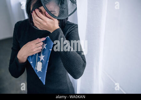 Crying woman holding dog tag et plié drapeau américain à la maison Banque D'Images