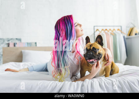 Fille aux cheveux colorés mignons petits animaux bouledogue français et à la recherche, tandis que dans le lit de pose Banque D'Images