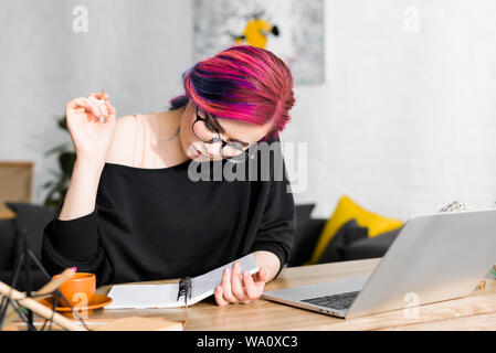 Fille aux cheveux colorés assis à table et la rédaction de notes dans l'ordinateur portable Banque D'Images