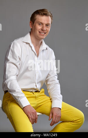 Portrait en gros plan d'un jeune homme de belle allure le gingembre dans une élégante chemise blanche et un pantalon jaune regardant la caméra et sourit tout en se posant sitti Banque D'Images