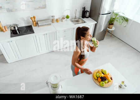 Overhead view of woman drinking smoothie près de fruits en cuisine Banque D'Images