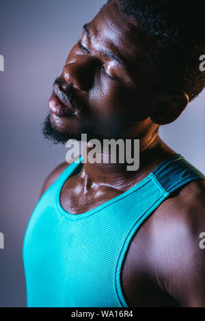 Portrait of african american sportsman avec visage en sueur et les yeux fermé sur fond gris avec éclairage Banque D'Images