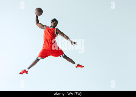 African American sportsman saute tout en jouant au basket-ball isolé sur gray Banque D'Images