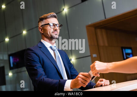 Handsome businessman en costume et lunettes donnant une carte de crédit pour femme Banque D'Images