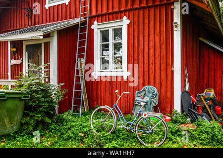 Les débris et les objets laissés à l'extérieur d'un rouge rustique ranch house y compris une bicyclette, des chaises empilées et une échelle dans le village de Porvoo, Finlande Banque D'Images