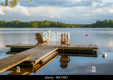 Deux chaises en bois au coucher du soleil sur une jetée sur les rives de la calme Saimaa lakein Finlande - 4 Banque D'Images