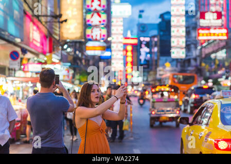 Bangkok, Thaïlande : 2 touristes admiratifs, qui vient d'arriver en taxi, tirer avec leur téléphone mobile nuit beauté de Yaowarat Road, Chinatown de nuit. Banque D'Images