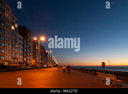 Un couple en train de marcher le long de la promenade du bord de mer d'Ostende (Oostende en anglais) après le coucher du soleil par sa plage de la mer du Nord, Flandre occidentale, Belgique. Banque D'Images