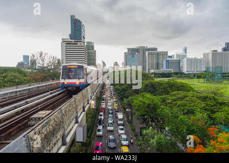 Bangkok - 9 juin 2019 : un train arrive à la gare BTS Ratchadamri pendant la pluie, au-dessus de l'embouteillage dans la rue avec les édifices du centre-ville. Banque D'Images