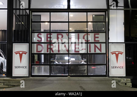 Entrée du centre de service Tesla Drive-In dans la nuit avec un modèle Tesla 3 derrière la porte. Banque D'Images