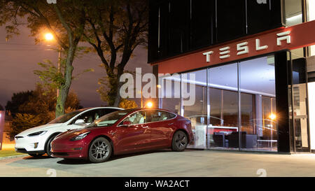 Modèle 3 Tesla rouge et blanc Tesla Model X stationné hors-avant d'un showroom Tesla dans la nuit. Banque D'Images