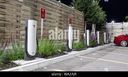 Tesla Supercharger Gare vu par une nuit claire avec Tesla Model S rouge à l'arrière-plan de charge. Banque D'Images