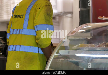 Un travailleur de la construction avec un gilet à bandes réfléchissantes pour un déjeuner auprès d'un restaurant local. Banque D'Images