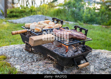 Steak et les pétoncles grillées sur un hibachi comme la fumée et les flammes se développent à partir de charbon chaud sur une soirée d'été ensoleillé Banque D'Images