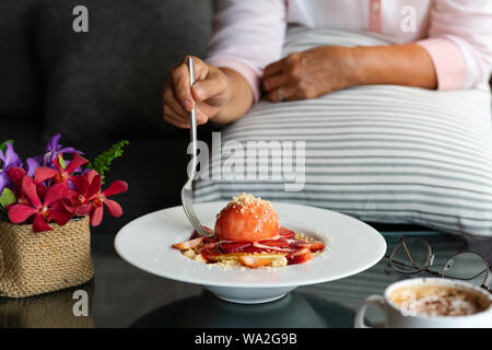 La vieille femme tient du folk avec des crêpes fraîchement faites maison, la Crumble aux fraises sur la plaque de dessert blanche Banque D'Images
