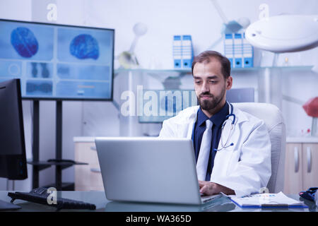 Un médecin travaillant sur son ordinateur portable assis à son bureau dans l'hôpital laboraty. Médecin de la saisie sur ordinateur portable. Jeune médecin en blouse blanche. Banque D'Images