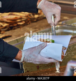 Chef avec des gants en caoutchouc et d'hygiène d'une paire de pinces prépare un rouleau de poissons à partir d'un rouleau, un morceau de filet de maquereau et une salade avec des oignons. Banque D'Images