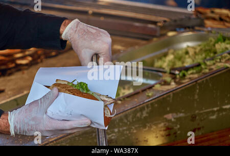 Chef avec des gants en caoutchouc et d'hygiène d'une paire de pinces prépare un rouleau de poissons à partir d'un rouleau, un morceau de filet de maquereau et une salade avec des oignons. Banque D'Images