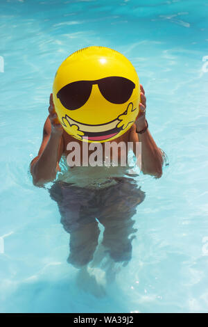 L'homme est faisant l'amusement dans la piscine gonflable, ballon jaune en face de son visage Banque D'Images