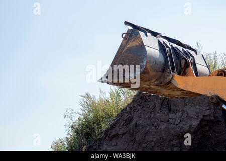 Le godet du tracteur libre efface le sol pour construction ultérieure sur le fond de ciel. L'arrière-plan. Place pour le texte. Banque D'Images