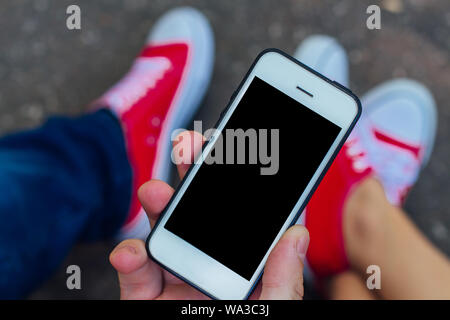 Main tenant le téléphone mobile à l'écran sur fond de blacj red sneakers chaussures femme et homme d'oie. Chaussures Chaussures de couple. Copier l'espace. Banque D'Images