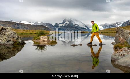 Randonneur marche sur des pierres dans l'eau, lac Stellisee, nuageux Matterhorn, Valais, Suisse Banque D'Images
