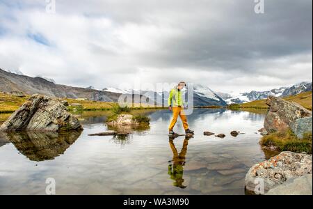 Randonneur marche sur des pierres dans l'eau, lac Stellisee, nuageux Matterhorn, Valais, Suisse Banque D'Images