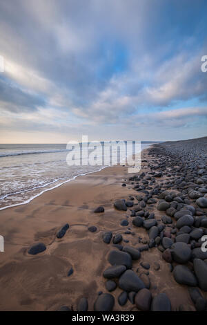 Vue portrait de Westward Ho ! Plage dans le Nord du Devon, près de coucher du soleil. Vous pouvez voir les vagues déferler sur le sable de la plage. Banque D'Images