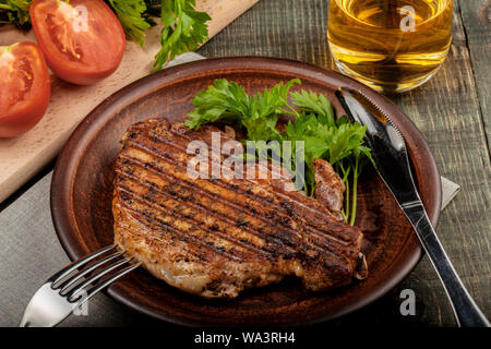 Sur une table de bois sur un plat blanc se trouve un morceau de porc frit avec des herbes, vue rapprochée Banque D'Images