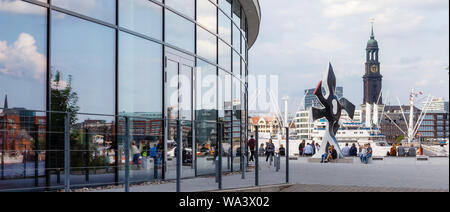 Hambourg, Allemagne. 14Th Aug 2019. Les passants s'asseoir à la sculpture 'La Grande fleur qui marche' de l'artiste Fernand Léger au musical pier "Roi des Lions". Dans l'arrière-plan vous pouvez voir l'église principale (St Michel l'Michel). Photo : Markus Scholz/dpa/Alamy Live News Banque D'Images