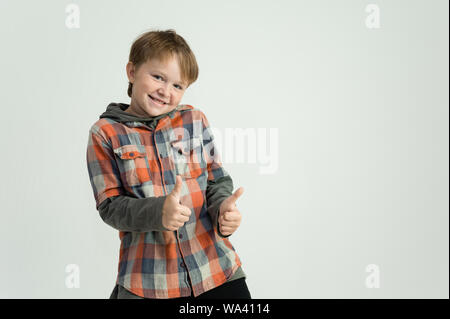 Portrait Photo taille-haute d'une joyeuse fun heureux mignon garçon d'âge scolaire. Se réjouit, sourires sur un fond blanc. Montre des mains. Banque D'Images