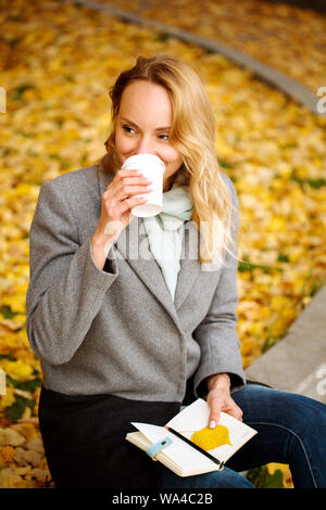Femme créative heureux avec bloc-notes papier boire du café en plein air dans le parc de l'automne avec les feuilles d'or Banque D'Images